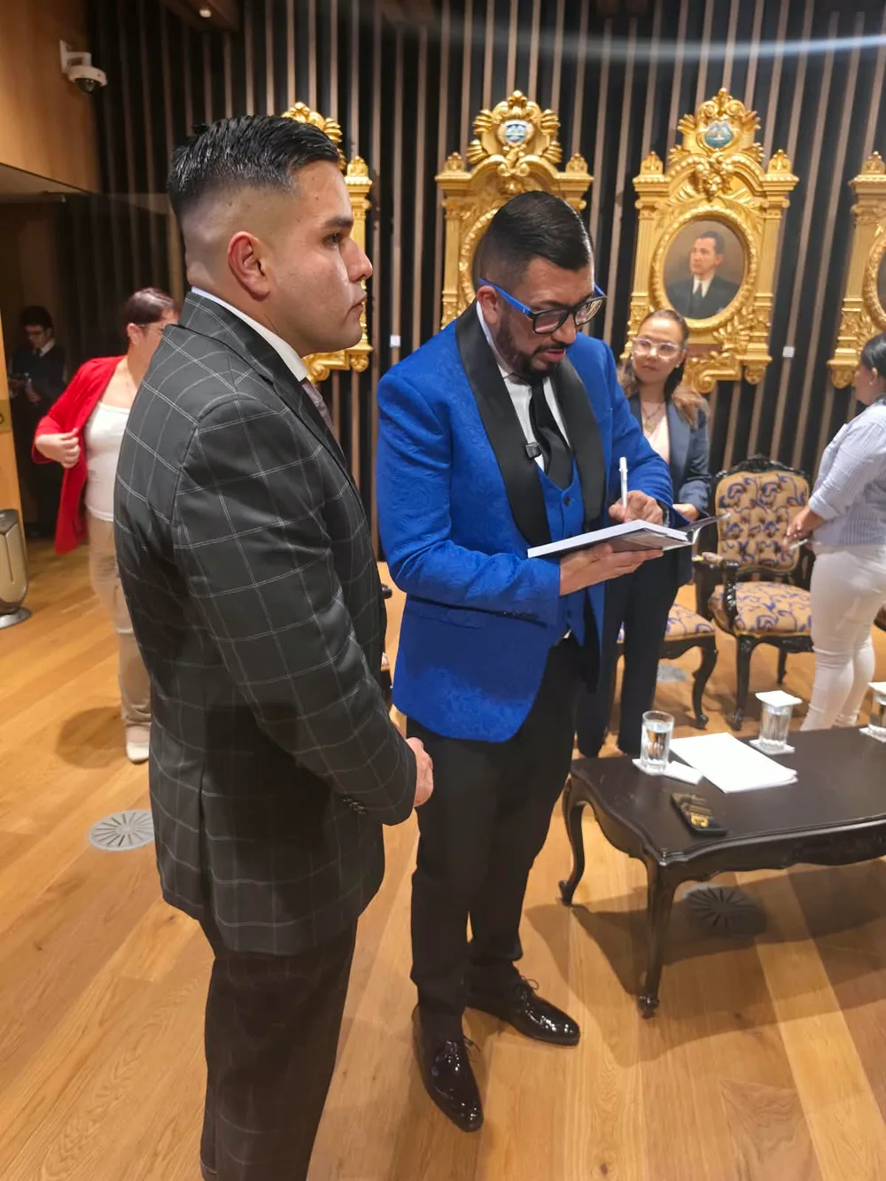 Joseph Rivera Cheves dedica un ejemplar de su libro sobre el femicidio de Nadia Peraza mientras un asistente espera, durante la presentación en la Asamblea Legislativa